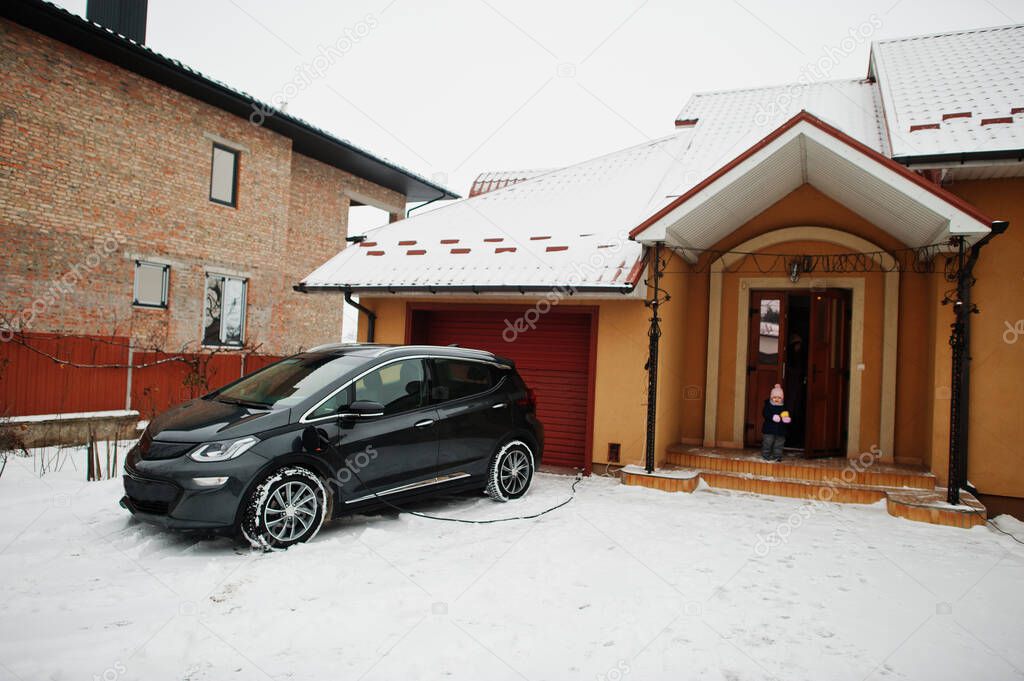 Charging electric car in the yard of house at winter.