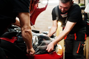 Araba servisi çalışanı, araba tamirhanesindeki kırmızı bir arabanın üzerine çakıl önleyici film koymuş. Özel filmli araba koruması.
