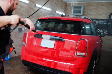 Garajda kırmızı araba yıkayan bir işçi..