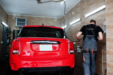 Garajda kırmızı araba yıkayan bir işçi..