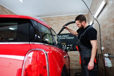 Yıkandıktan sonra garajda kırmızı arabayı kurutan bir işçi..