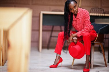 Pretty braids business african american lady bright bossy person friendly wear office red shirt, hat and trousers, sit on chair.