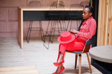 Pretty braids business african american lady bright bossy person friendly wear office red shirt, hat and trousers, sit on chair.