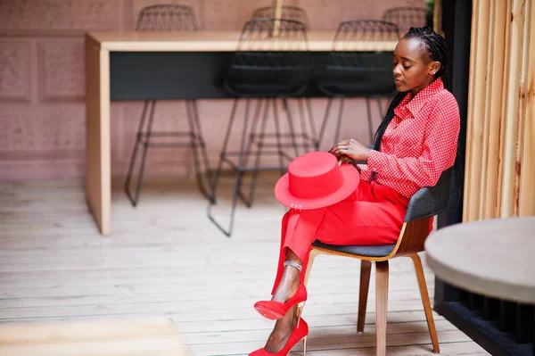 Pretty braids business african american lady bright bossy person friendly wear office red shirt, hat and trousers, sit on chair.