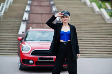 Şapkalı, siyah, mavi korseli, kırmızı şehir arabasının yanında parlak makyajlı güzel, sarışın, seksi kadın modelin portresi.. 