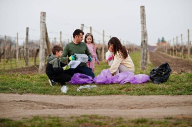 Üzüm bağlarını temizlerken çöp torbası toplayan bir aile. Çevresel koruma ve ekoloji, geri dönüşüm.