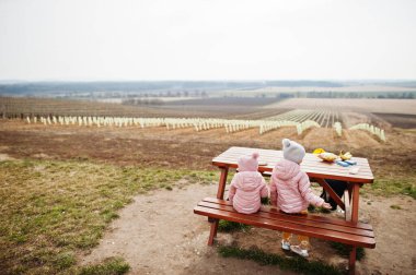 İki küçük kızın arkası, üzüm bağına karşı ahşap masada oturuyor..