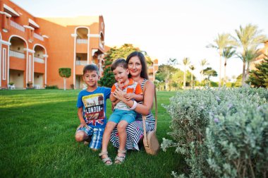 Mısır tatil köyünde yeşil çimlerde oturan iki oğlu olan bir anne. Aile tatili.