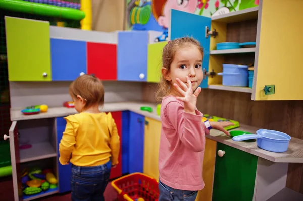 Cute sisters playing in indoor play center. Kindergarten or preschool play room. In the children\'s kitchen.