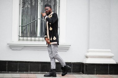 Geleneksel ceket giymiş mega stil Afrikalı bir adam. Şapkalı, güneş gözlüklü, elinde puro olan şık siyahi bir adam..