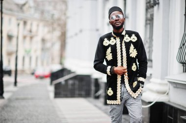 Geleneksel ceket giymiş mega stil Afrikalı bir adam. Şapkalı, güneş gözlüklü, elinde puro olan şık siyahi bir adam..