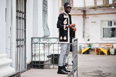 Geleneksel ceket giymiş mega stil Afrikalı bir adam. Şapkalı, güneş gözlüklü, elinde puro olan şık siyahi bir adam..