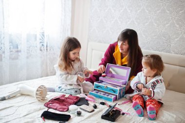 Mother and daughters doing makeup on the bed in the bedroom.