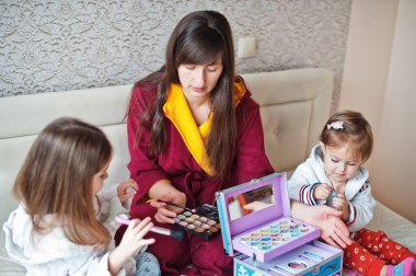 Mother and daughters doing makeup on the bed in the bedroom.