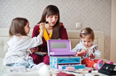 Mother and daughters doing makeup on the bed in the bedroom.