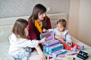 Mother and daughters doing makeup on the bed in the bedroom.
