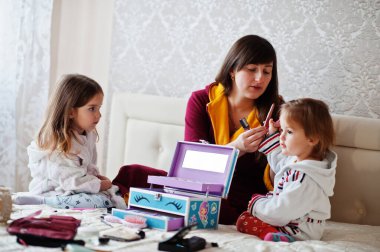 Mother and daughters doing makeup on the bed in the bedroom.