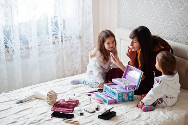 Mother and daughters doing makeup on the bed in the bedroom.