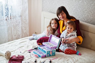 Mother and daughters doing makeup on the bed in the bedroom.