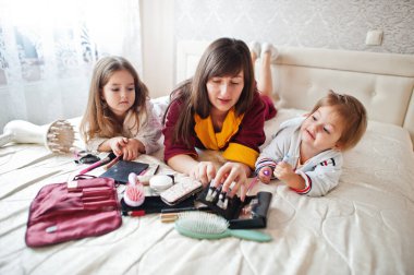 Mother and daughters doing makeup on the bed in the bedroom.