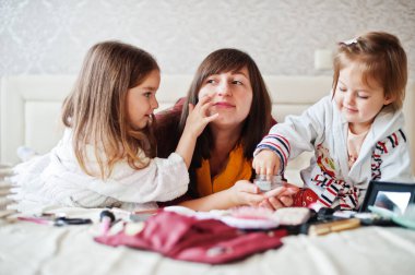 Mother and daughters doing makeup on the bed in the bedroom.