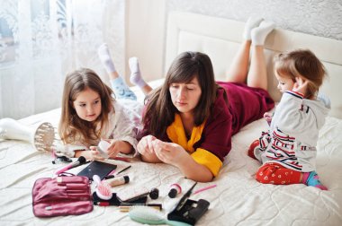 Mother and daughters doing makeup on the bed in the bedroom.