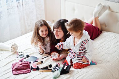 Mother and daughters doing makeup on the bed in the bedroom.