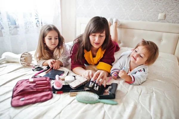 Mother and daughters doing makeup on the bed in the bedroom.