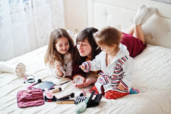 Mother and daughters doing makeup on the bed in the bedroom.