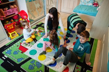 Mutlu bir aile birlikte eğleniyor, dört çocuk ve bir anne evde twister oynuyor..