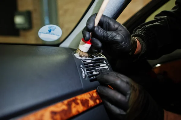 Man in uniform and respirator, worker of car wash center, cleaning car interior cleaning brush . Car detailing concept.