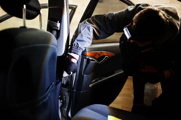 Man in uniform and respirator, worker of car wash center, cleaning car interior cleaning brush . Car detailing concept.