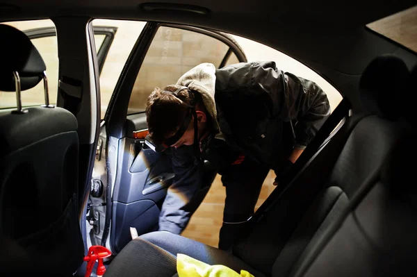 Man in uniform and respirator, worker of car wash center, cleaning car interior cleaning brush . Car detailing concept.