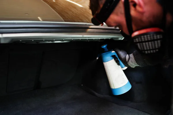 Man in uniform and respirator, worker of car wash center, cleaning car interior with hot steam cleaner. Car detailing concept.