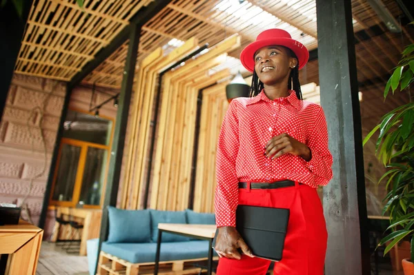 Pretty braids business african american lady bright bossy person friendly wear office red shirt, hat and trousers, hold tablet on hands.