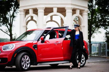 Şapkalı, siyah, mavi korseli, kırmızı şehir arabasının yanında parlak makyajlı güzel, sarışın, seksi kadın modelin portresi.. 