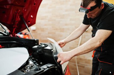 Araba servisi çalışanı, araba tamirhanesindeki kırmızı bir arabanın üzerine çakıl önleyici film koymuş. Özel filmli araba koruması.