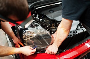 Araba servisi çalışanı, araba tamirhanesindeki kırmızı bir arabanın üzerine çakıl önleyici film koymuş. Özel filmli araba koruması.