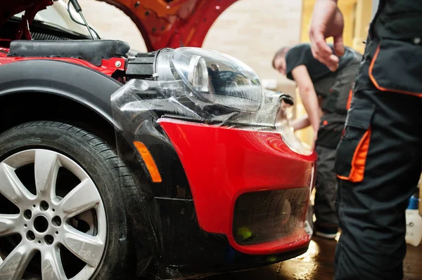 Araba servisi çalışanı, araba tamirhanesindeki kırmızı bir arabanın üzerine çakıl önleyici film koymuş. Özel filmli araba koruması.