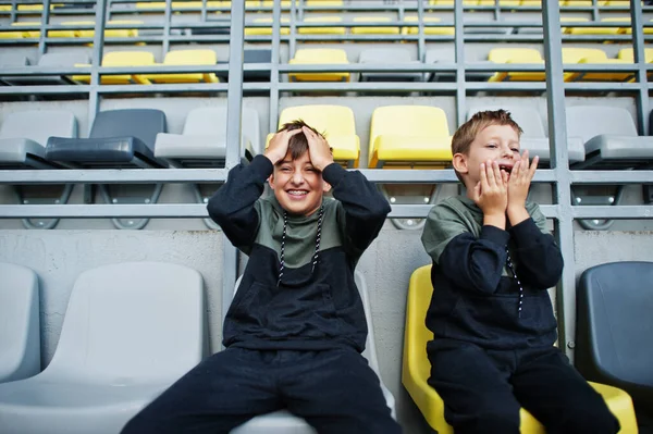 Oh no, they lost the game! Two brothers support their favorite team, sitting on the sports podium at the stadium.