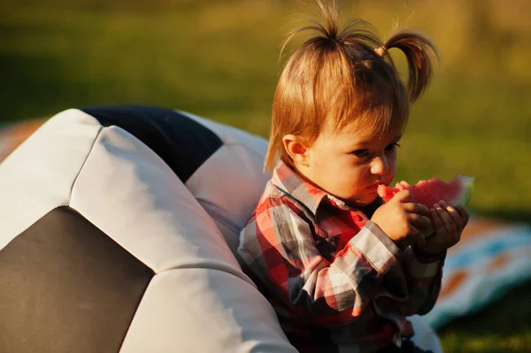 체크무늬 셔츠를 귀여운 아이가 축구공 주머니에 수박을 먹는다 — 스톡 사진