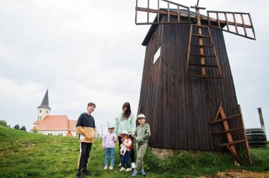 Mother with four kids stand near old wooden windmill.