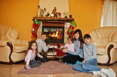 Kış günü sıcak oturma odasındaki şöminenin yanında mutlu, genç bir aile. Evde dört çocuklu bir anne..