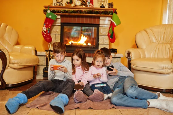 Happy Four Kids Watching Mobile Phone Home Fireplace Warm Living — 图库照片