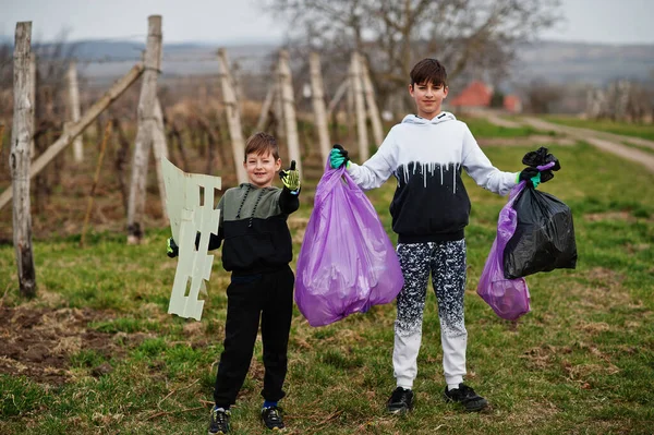 Brothers with trash bag collecting garbage while cleaning in the vineyards . Environmental conservation and ecology, recycling.