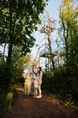 Family with kids against viewing tower at Brno, Czech Republic. Watchtower during sunset with trees.