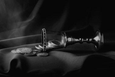 Aristokrat ortaçağ cam bardağında kristaller, elmaslar, para, madeni para. Tek renkli, lüks, eşsiz fotoğrafçılık. Büyüleyici. Kumaş ve duman. Servet, hazineler..