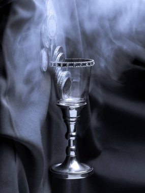 Şu resmin fotografı, büyülü. Orta Çağ 'daki cam bardak, kristaller, elmaslar ve gümüş saplı. Para havada uçuşuyor, arka planda sıcak bir duman var. Kumaşın arkaplan dokusu.