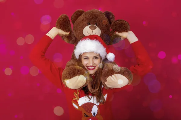 笑容满面的漂亮女人 肩上戴着圣爪帽 驯鹿毛衣和巨大的泰迪熊 — 图库照片