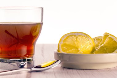 Tahta sehpanın üzerinde beyaz arkaplan, limon dilimleri ve çay kaşığı şeklinde cam karışımı. Çay saati konsepti